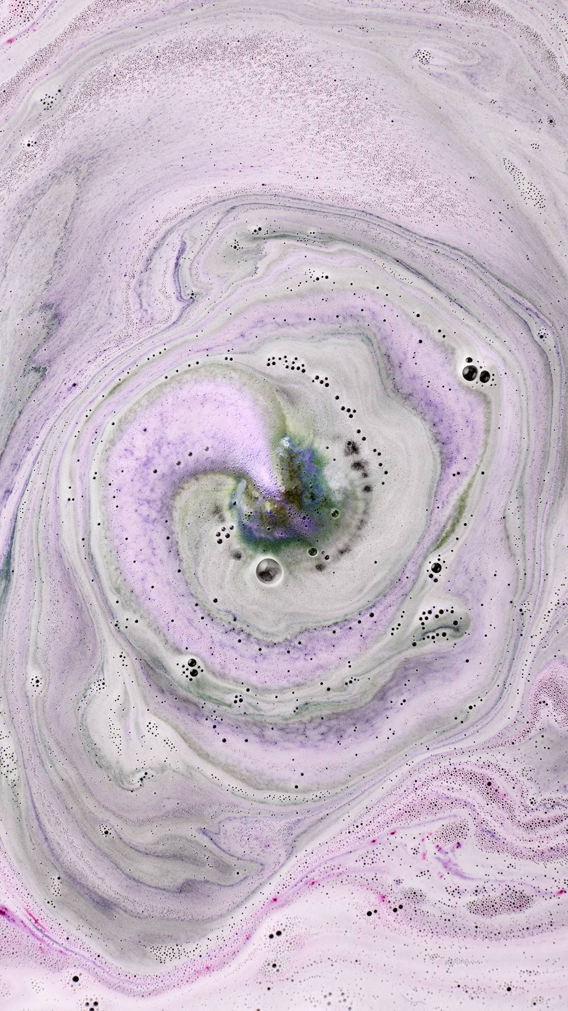 Black Rose. An aerial view shows the dark rose-shaped bath bomb as it has nearly fully dissolved. The water is a deep, velvety purple and pink, covered in a thick layer of shimmering silver plastic-free glitter and delicate bubbles.